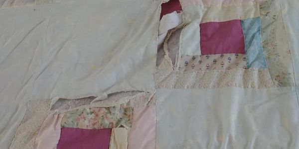 damaged and worn quilt displaying holes and spots where batting is showing.
