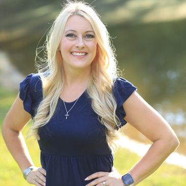 therapist standing outside in the sun by a pond smiling in a navy blue dress. 