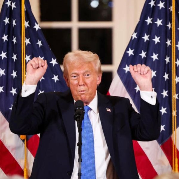 A man in a suit raises his fists with American flags behind him.