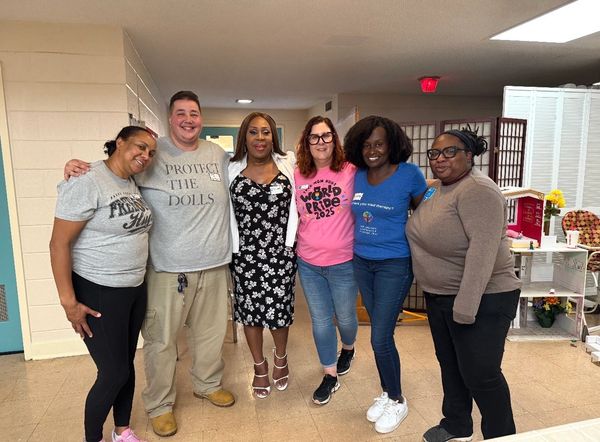 A diverse group of six people smiling and posing indoors.