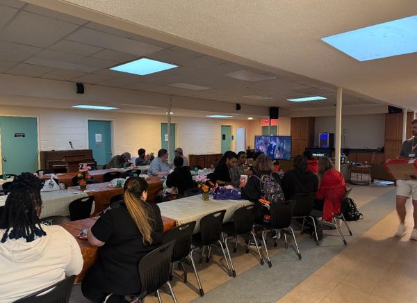 Group of people seated at tables in a community room watching TV.