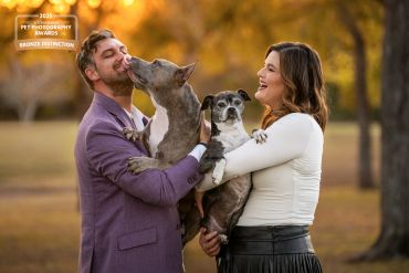 Couple joyfully holding two dogs outdoors in autumn.