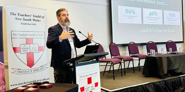 A man speaks at a podium during a Teachers' Guild of NSW event.
