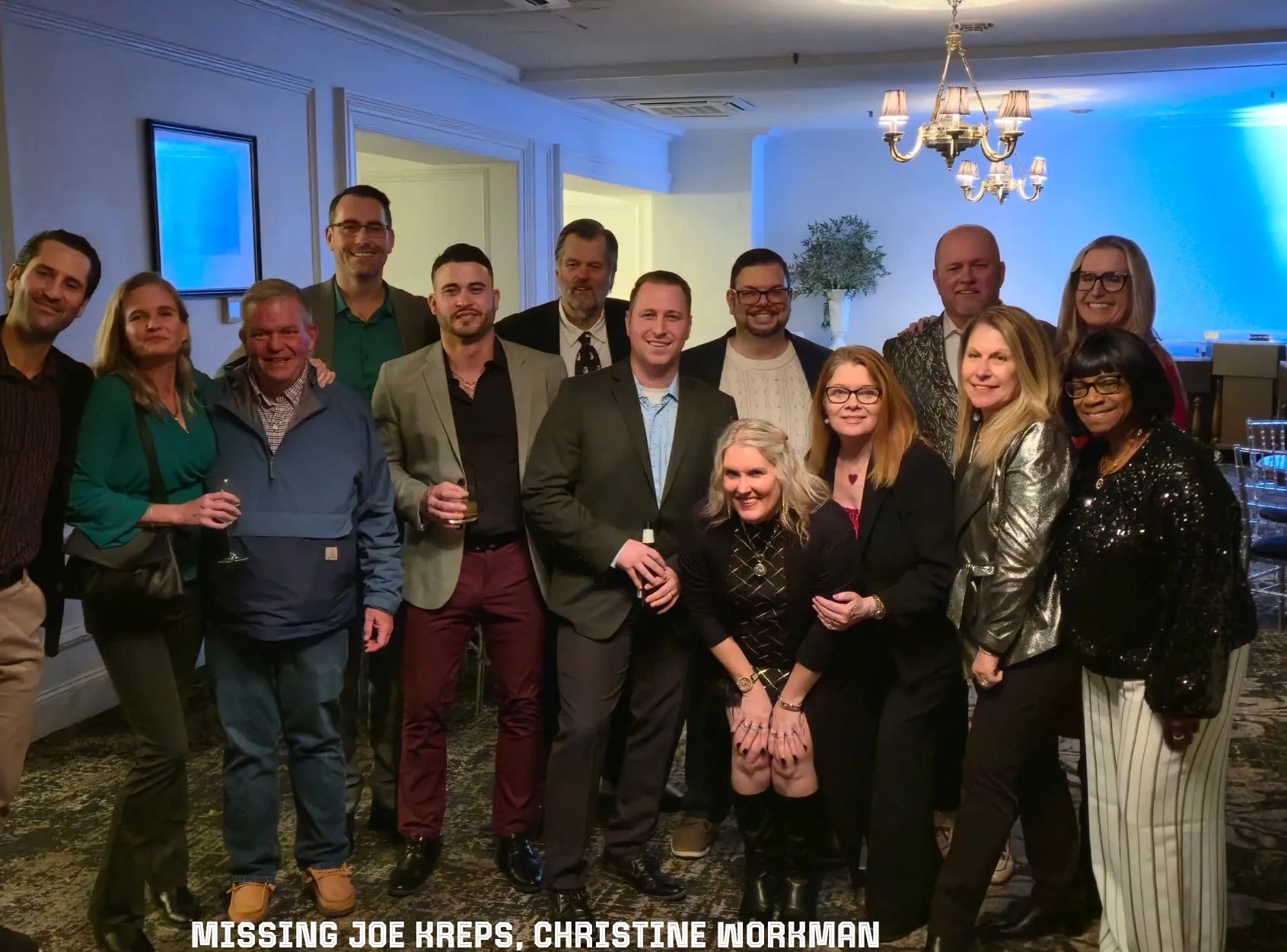Group photo of people at a social gathering indoors, smiling and holding drinks.