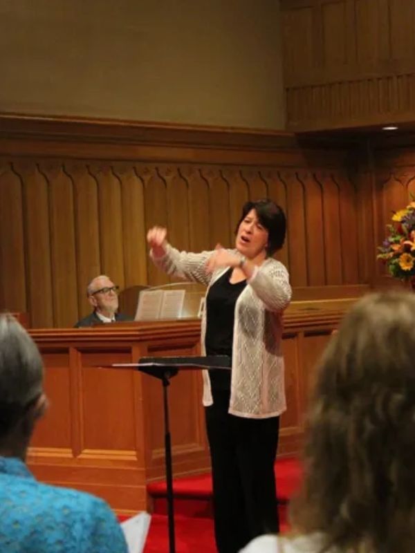 A woman passionately conducting music in a wooden-paneled hall.