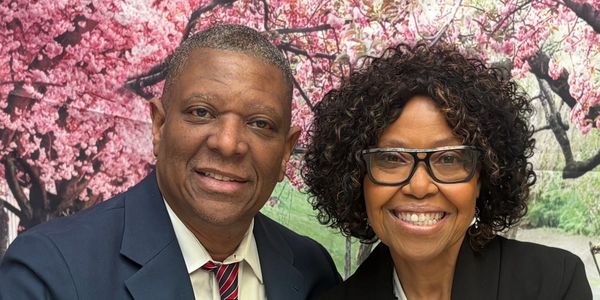Smiling man and woman posing in front of cherry blossom trees.