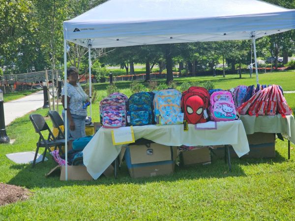 Woman selling colorful backpacks under a canopy outdoors.