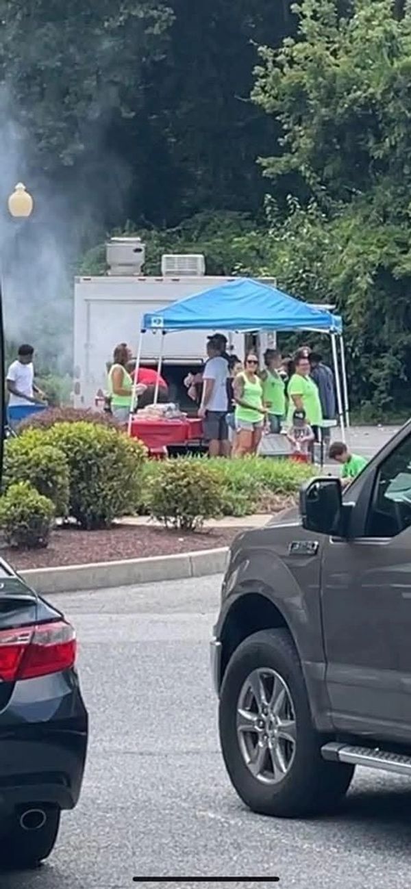Group gathers under blue canopy near food truck in parking lot.