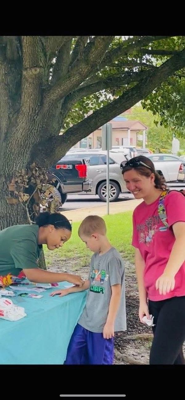 Child interacting with woman at table under tree.
