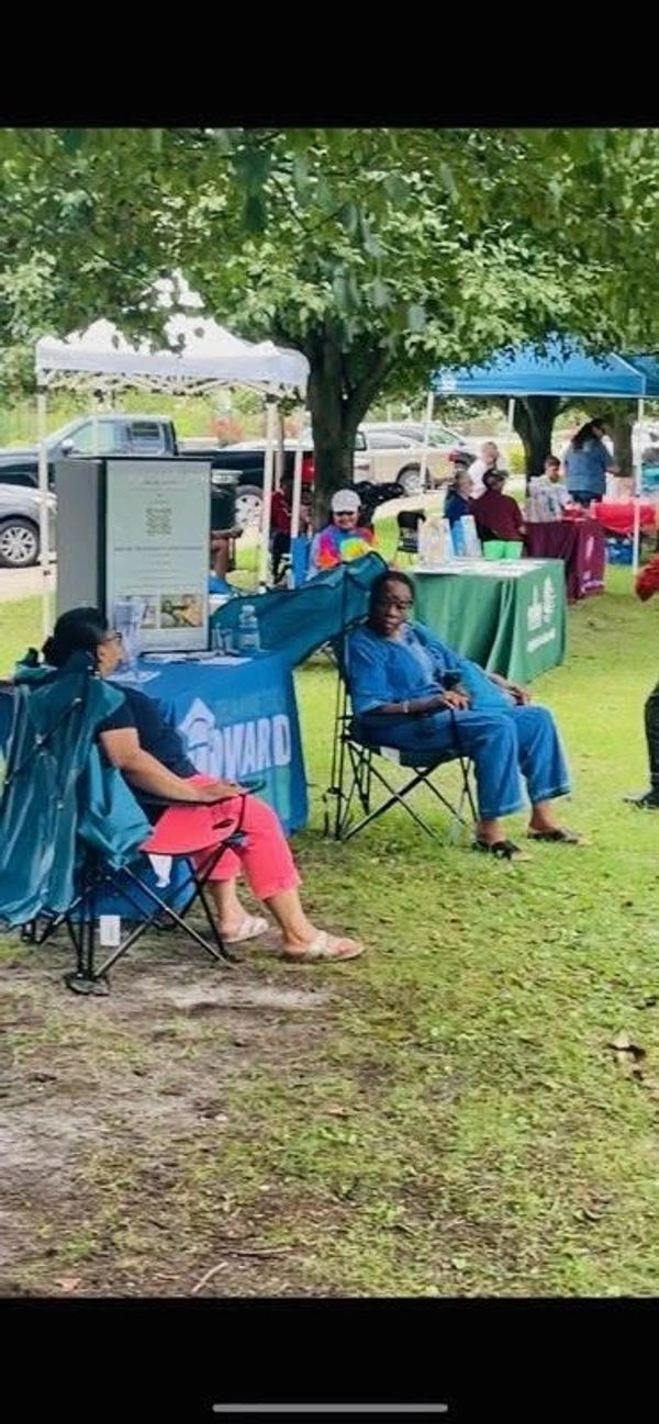 People sitting at an outdoor event with tents and tables under trees.