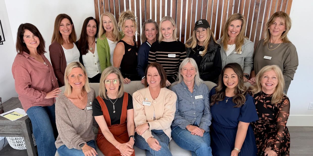 Group of 17 women smiling indoors, posing for a photo.