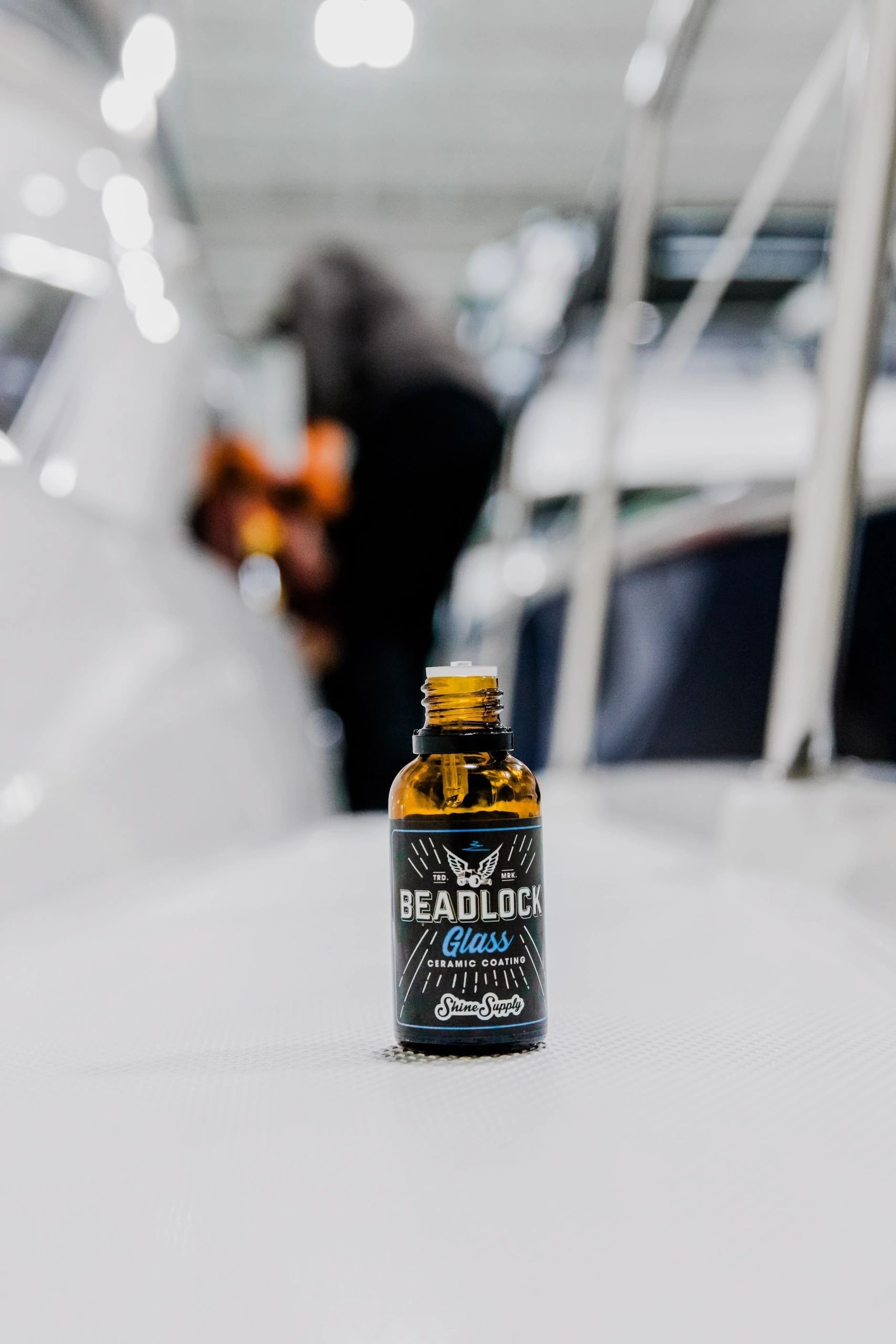 An open amber glass bottle labeled “Beadlock Glass Ceramic Coating” by Shine Supply sits on a light-