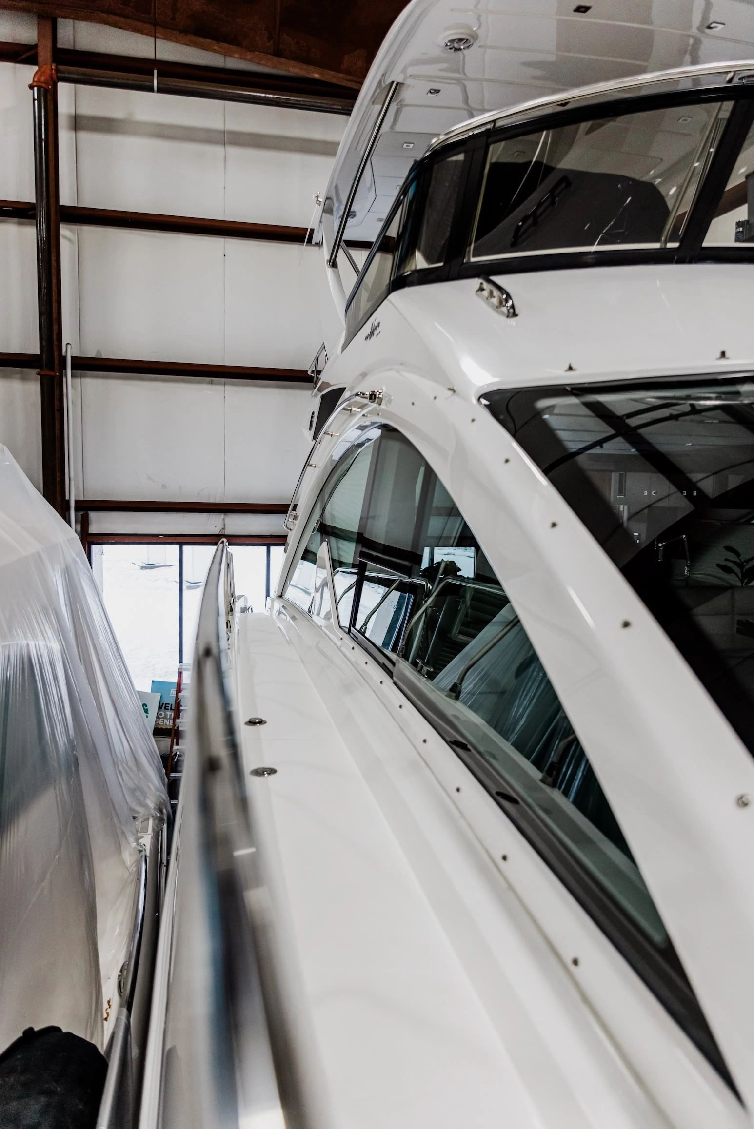 A close-up view of a white yacht hull inside an indoor marina or service facility, showing smooth ge