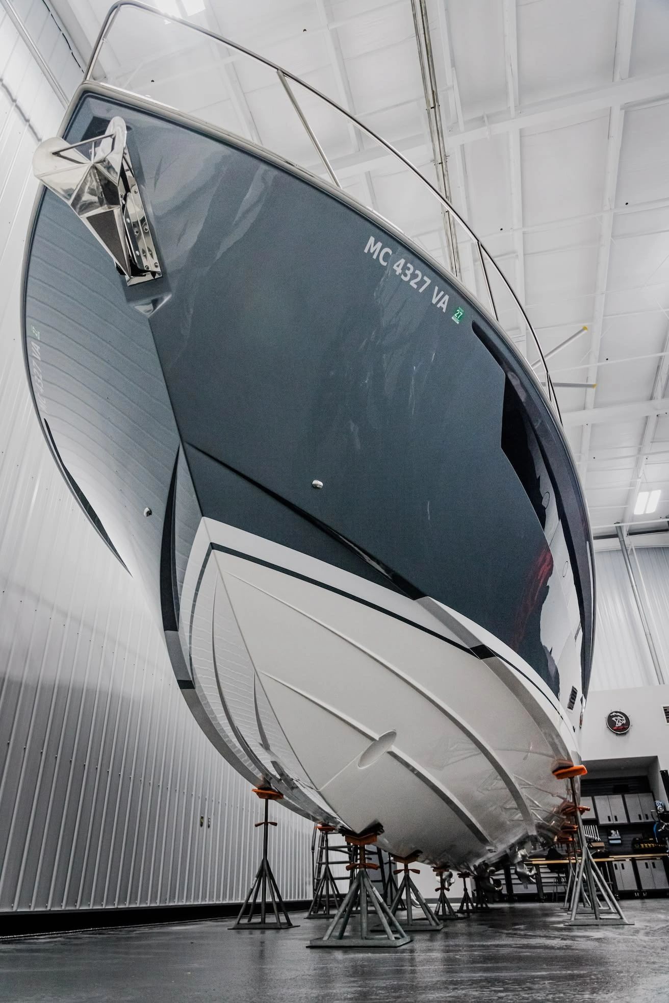 A large yacht hull elevated on stands inside an indoor service facility, showing a smooth, glossy fi