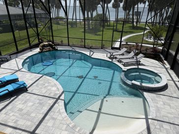 Screened-in backyard pool with lounge chairs and hot tub.