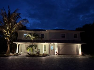 Well-lit modern two-story house at night with palm trees.