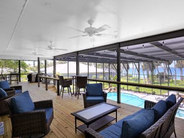 Spacious screened porch with comfortable seating overlooking a pool and waterfront view.