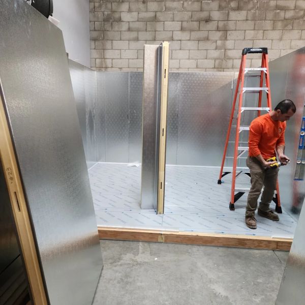 Man setting up metal panels with ladder in industrial space.