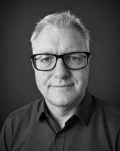 Black and white portrait of a middle-aged man wearing glasses and a buttoned shirt.