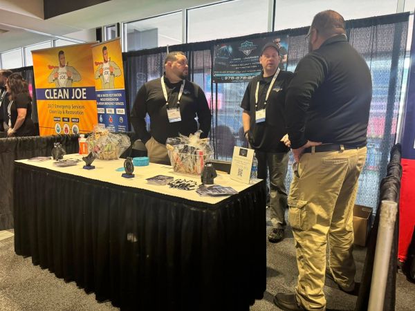 Three men in black shirts at a trade show booth for Clean Joe services.