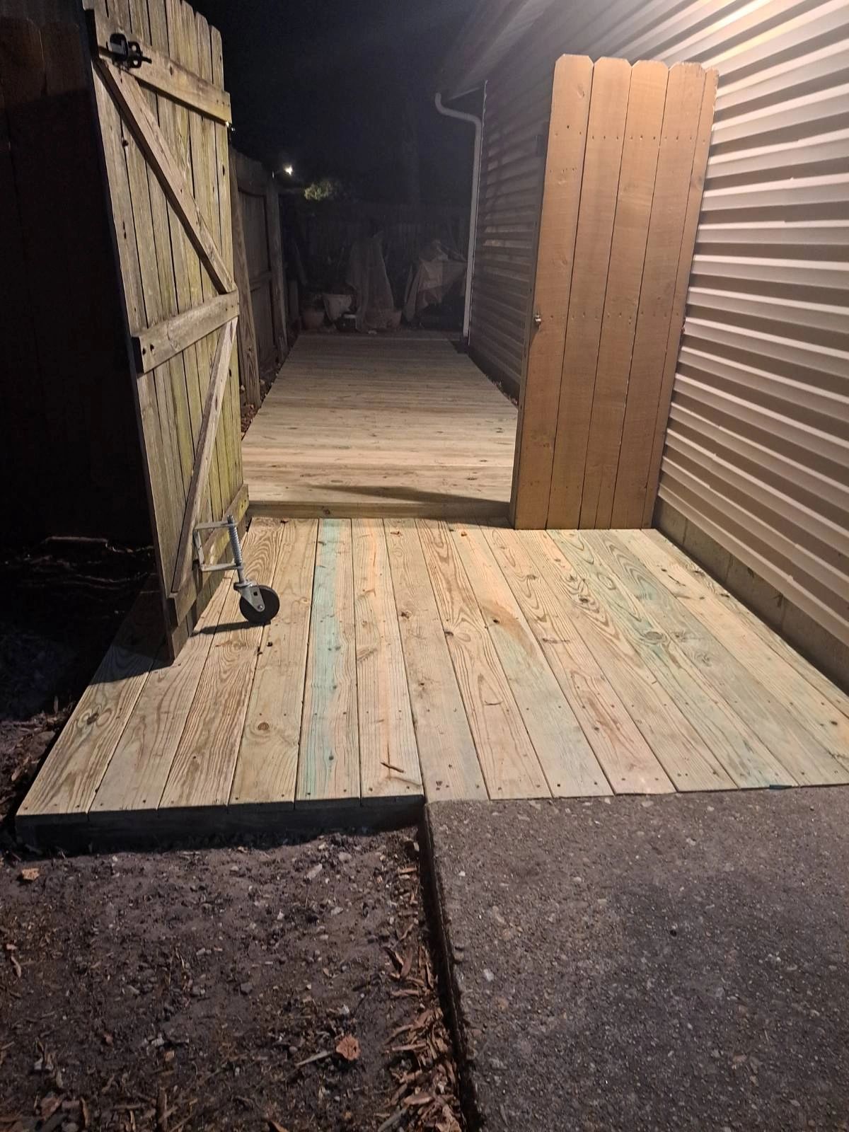 Wooden gate and deck illuminated at night beside a house.