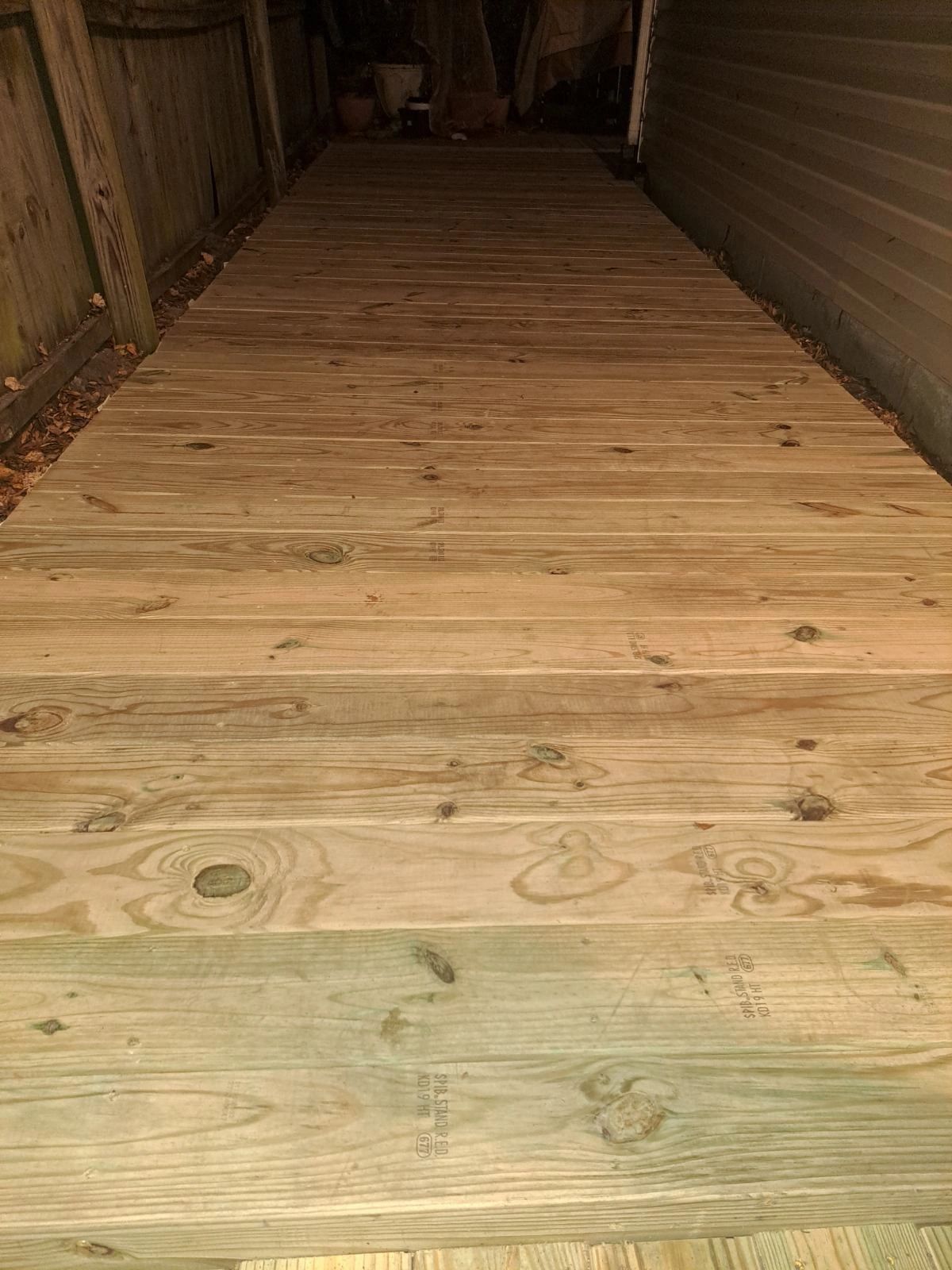 Newly installed wooden deck between a fence and house siding.