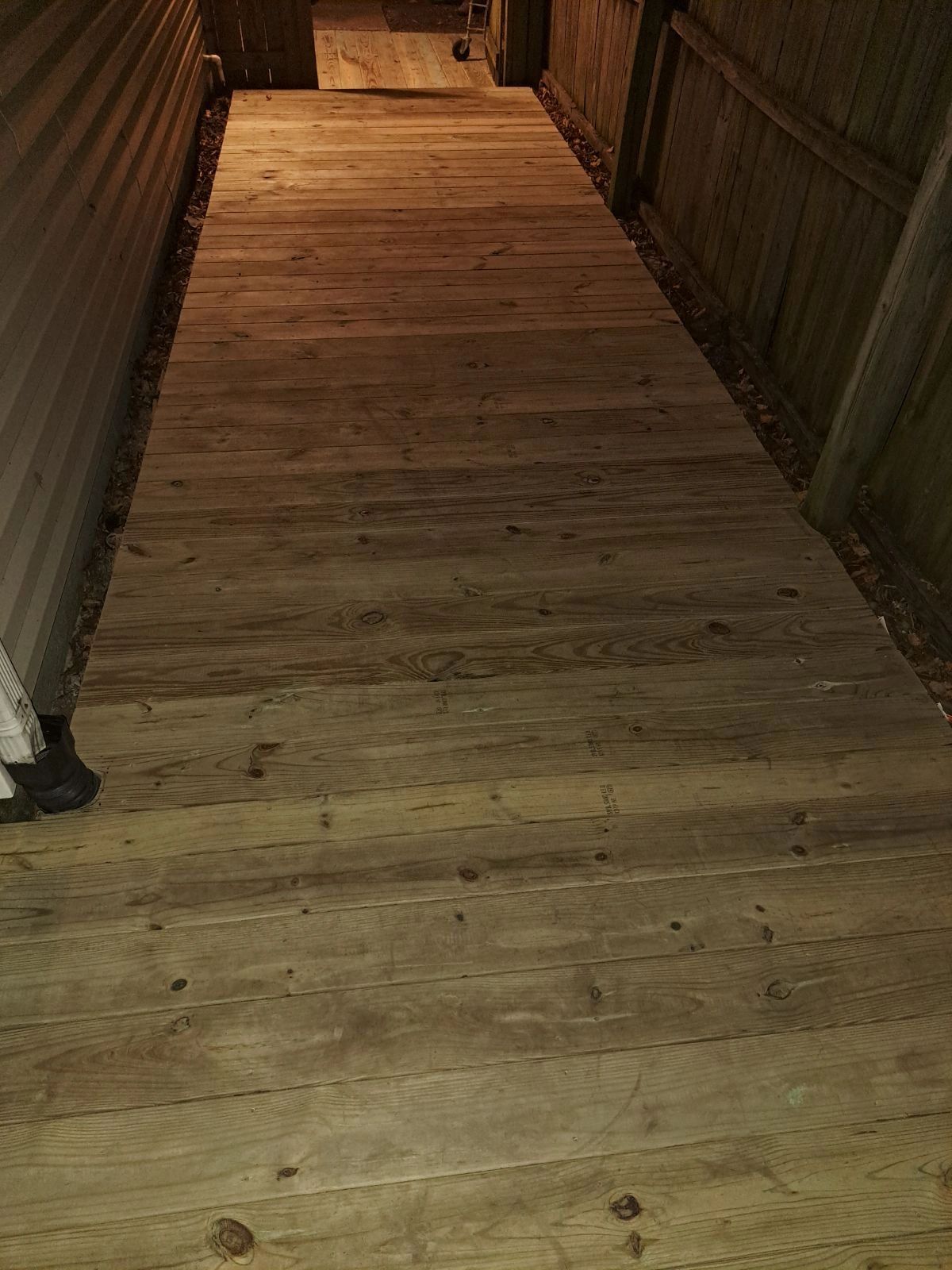 Wooden pathway between a house and a fence at night.