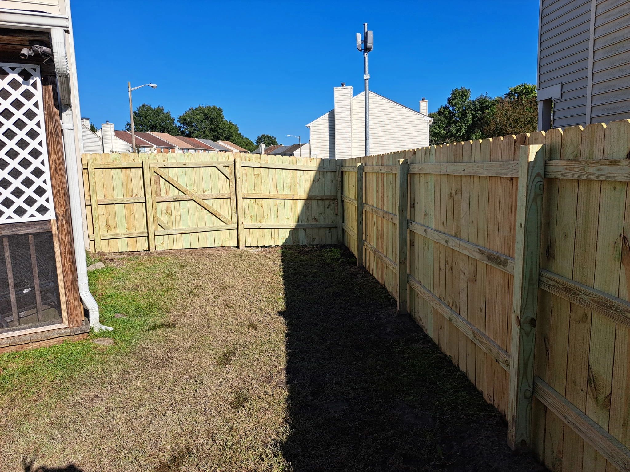 Newly installed wooden fence enclosing a small backyard area on a sunny day.