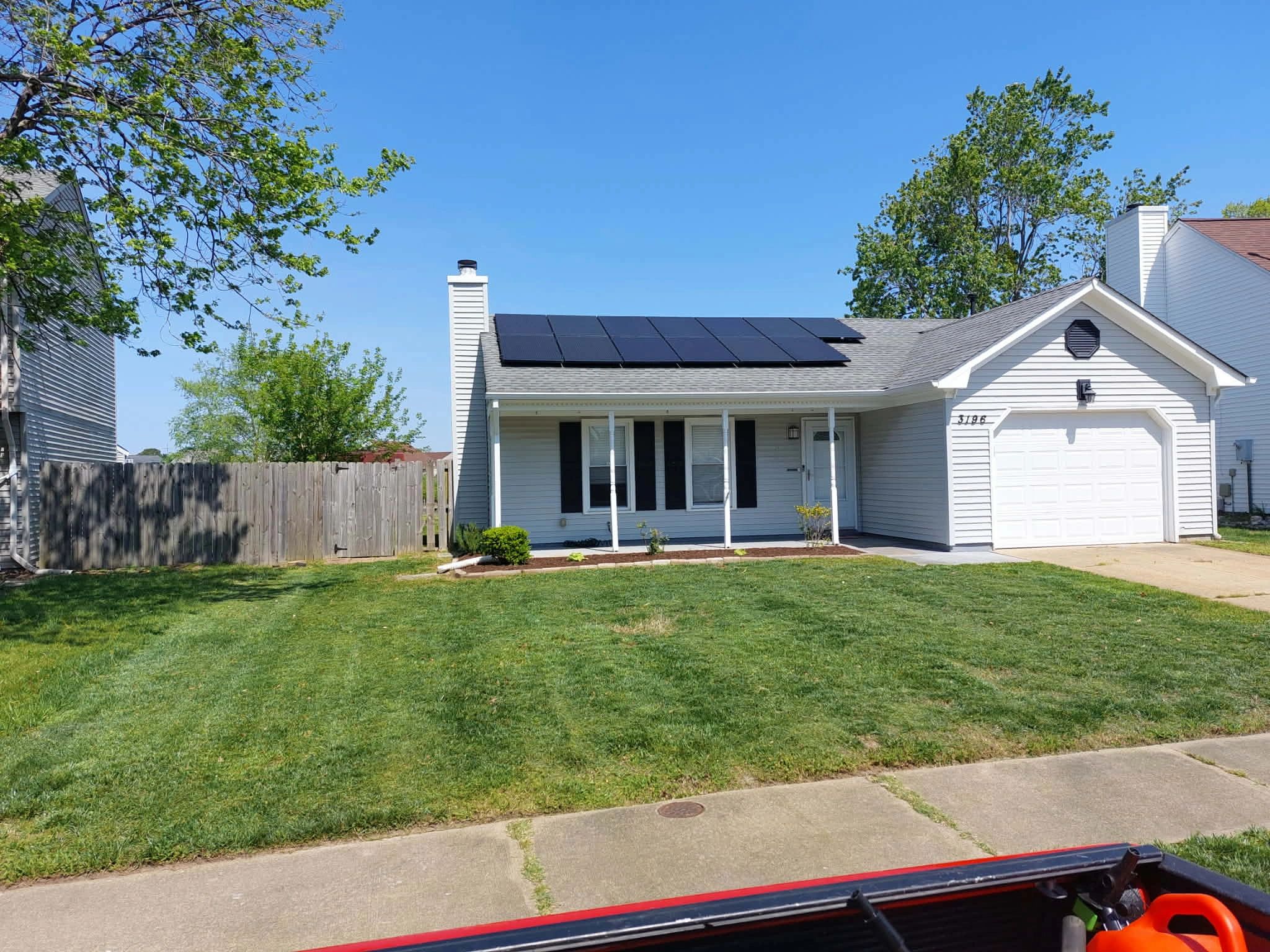 Single-story house with solar panels on the roof and a green lawn.