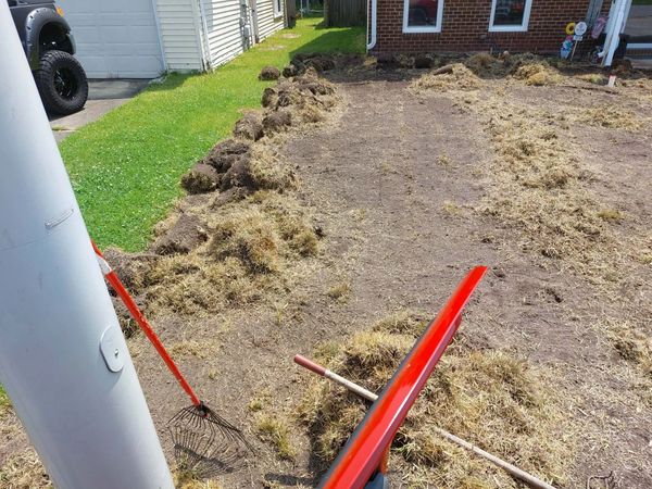 Yard with dug-up soil and garden tools near a house.