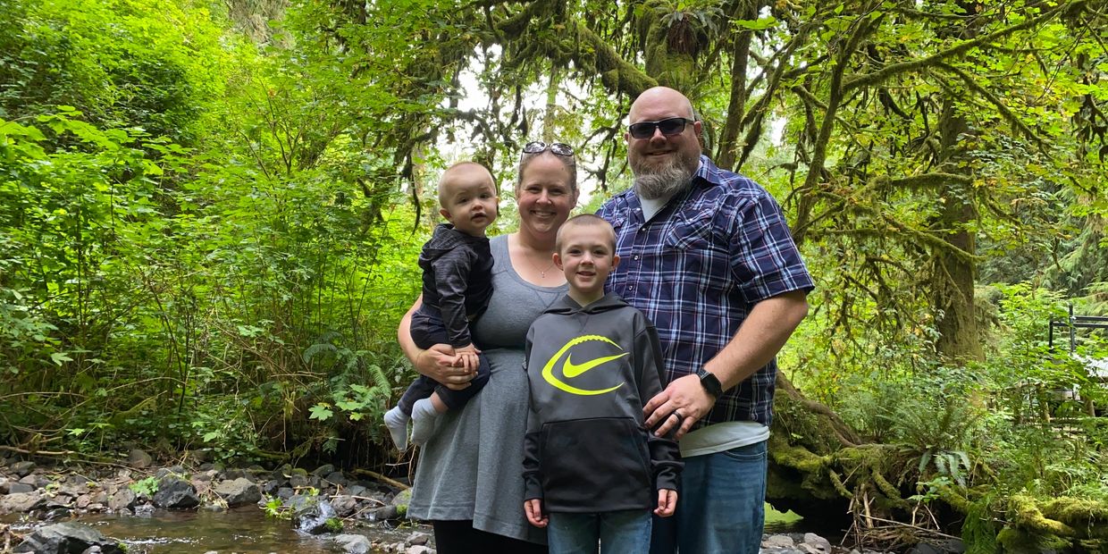 A family of four smiling in a lush forest by a creek.