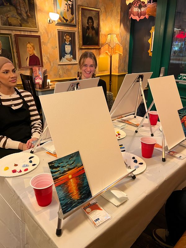 People enjoying a guided painting session in a cozy room with art decor.