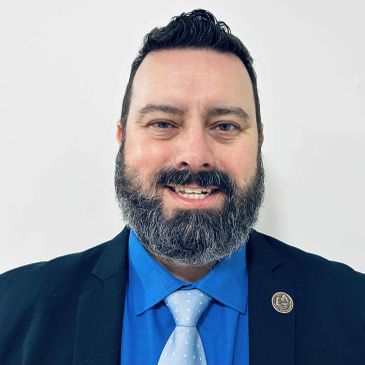 Smiling man with beard in suit and blue shirt.