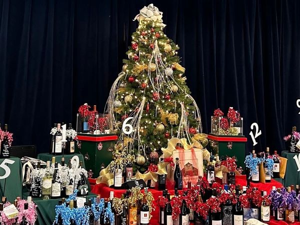 Decorated Christmas tree surrounded by wine bottles with colorful bows.