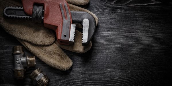 Professional plumbing wrench tool with leather glove and plumbing fittings on wood floor