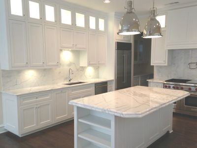 Modern white kitchen with marble countertops and island under pendant lights.
