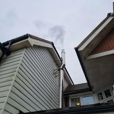 Smoke rising from a chimney on a residential house against a cloudy sky.
