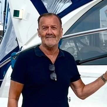 Man in black polo shirt standing near a boat.