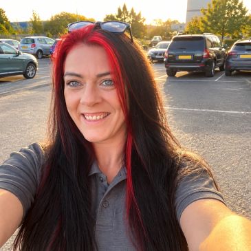 Woman with red and black hair takes a selfie in a parking lot at sunset.