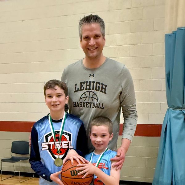 Coach with two young basketball players holding a ball and medals.