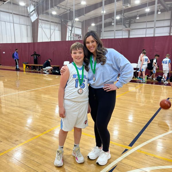 A boy and a woman proudly display their medals in a gymnasium.