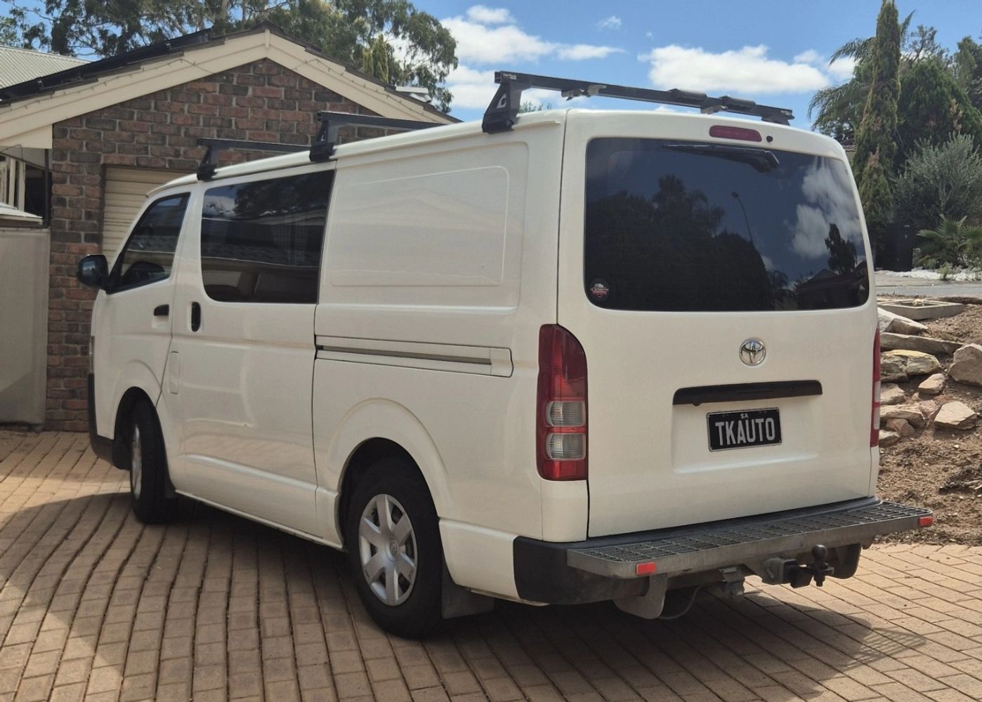 White Toyota van parked in a driveway beside a brick garage.