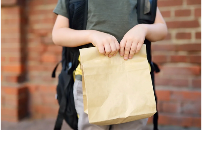 school boy holding paper lunch bag