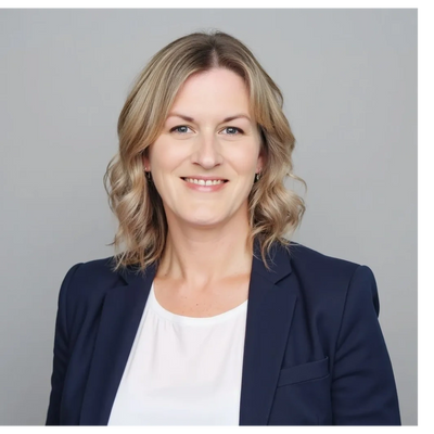 Professional woman with blonde hair in business attire smiling against a gray background.