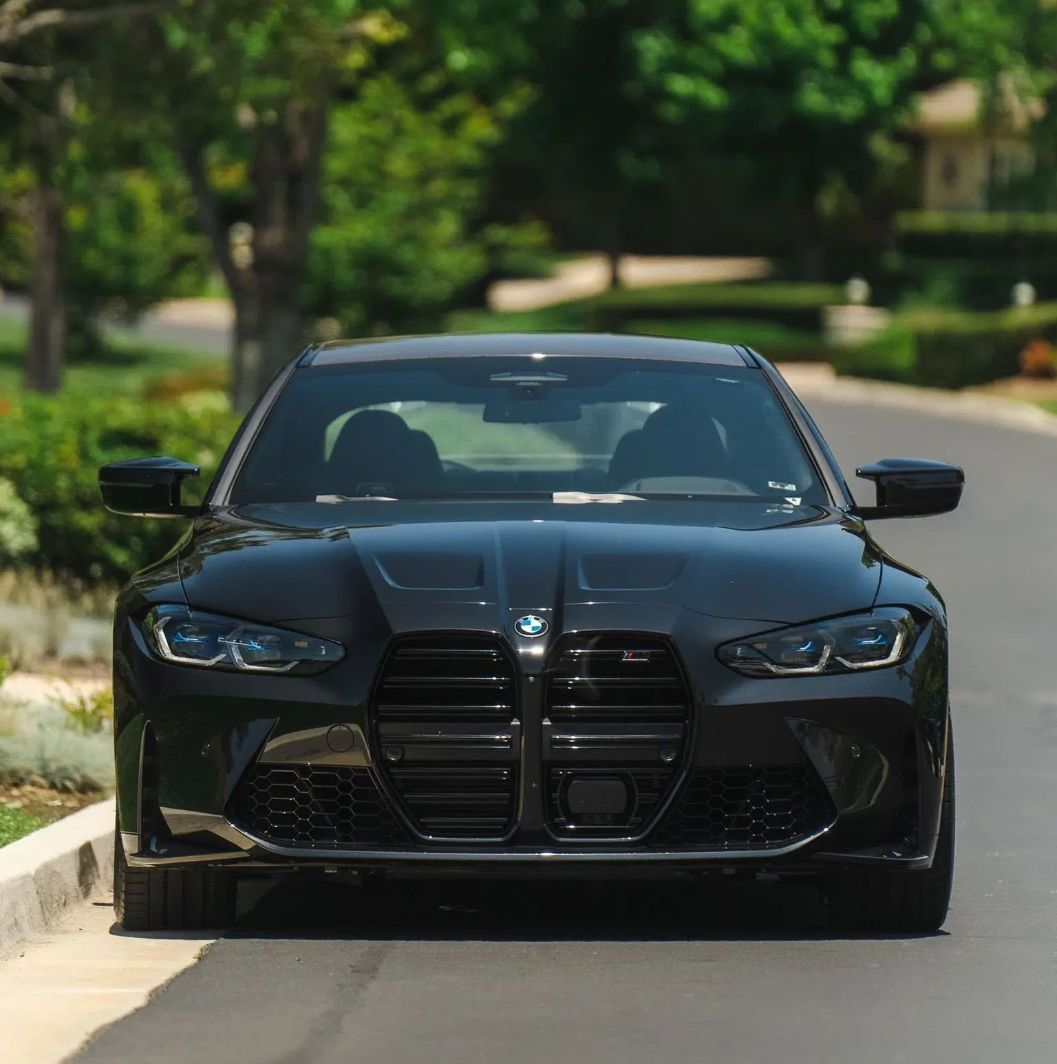 Front view of a sleek black BMW M4 on a sunny street.