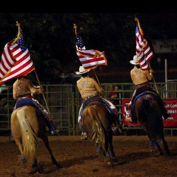 Three riders on horseback carrying American flags at night.