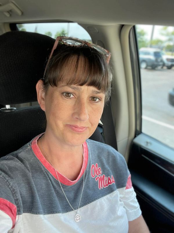 A woman wearing an Ole Miss shirt sits in a car, smiling softly.