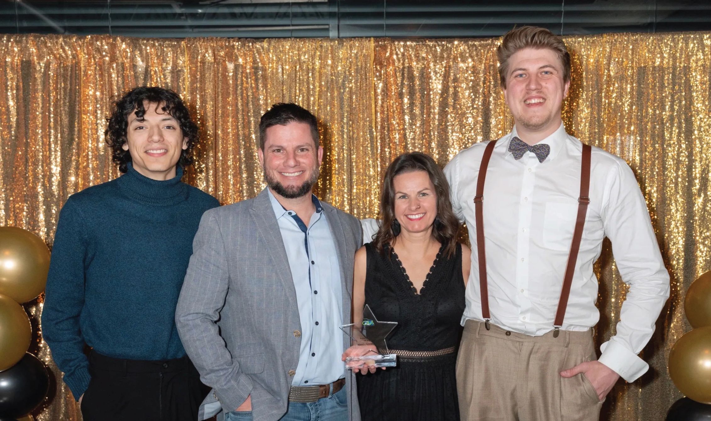 Four people posing happily with an award in front of a glittery gold backdrop.