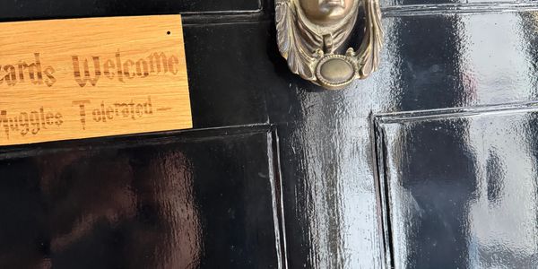 A wooden sign on a black door with a metallic knocker shaped like a face.