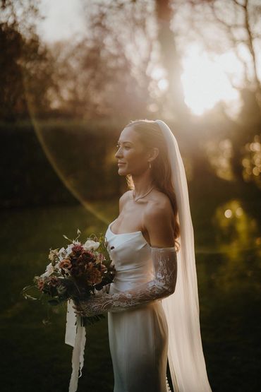 Bride in a white dress holding a bouquet in golden sunlight.